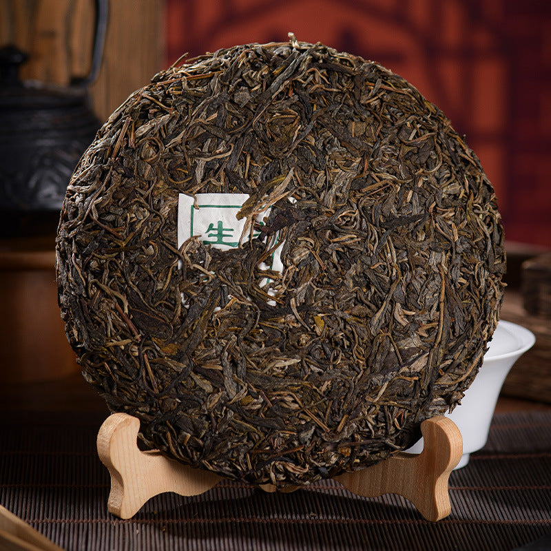 Unwrapped Lvshuitang raw pu-erh tea cake on wooden stand — compressed sheng puerh with internal ticket, Lincang Mengku Chinese tea, stone-pressed 357g
