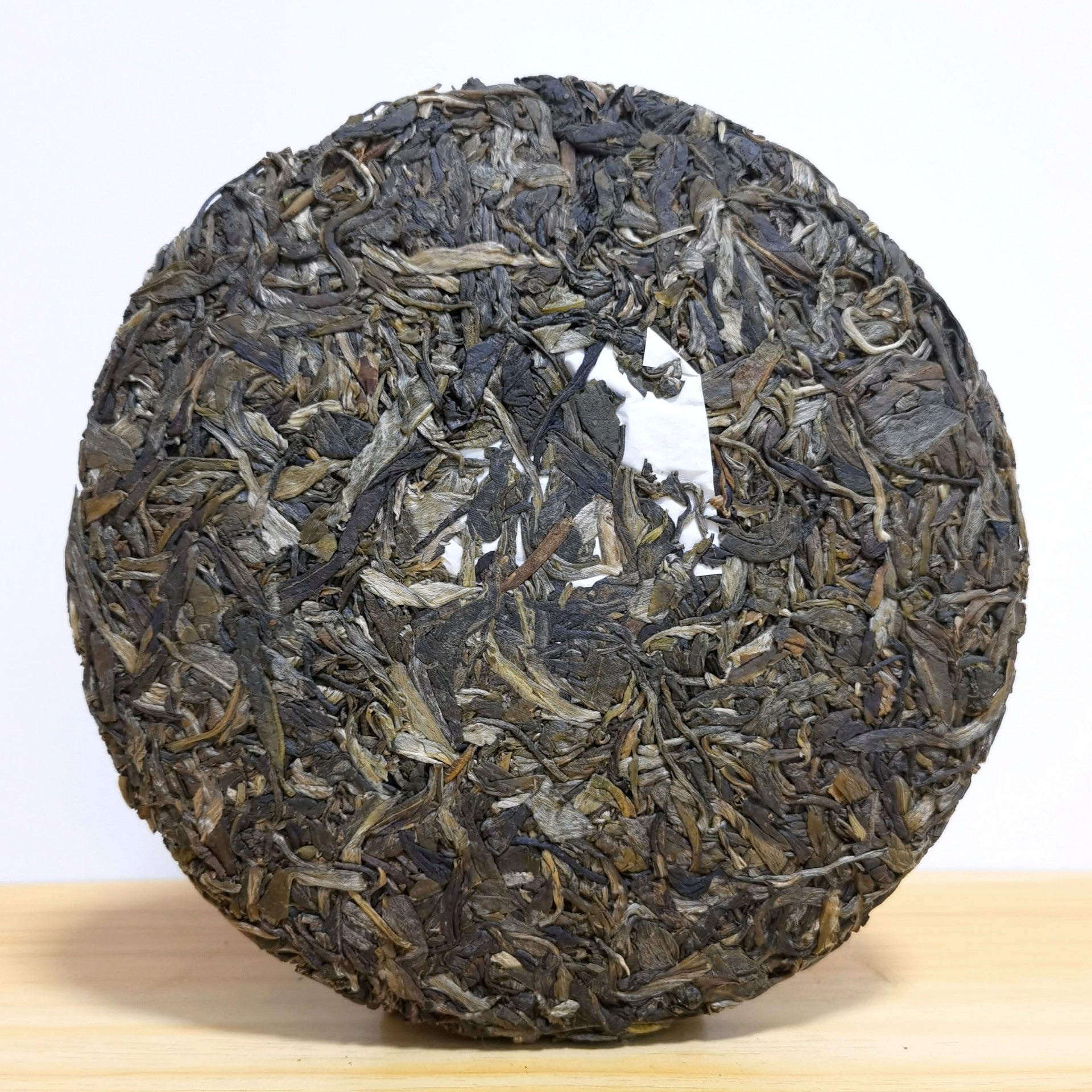 Top view of unwrapped Xigui raw pu-erh tea cake showing compressed leaves with internal ticket — Lincang Chinese sheng puerh, black thorn strips and silver buds, stone-pressed 357g
