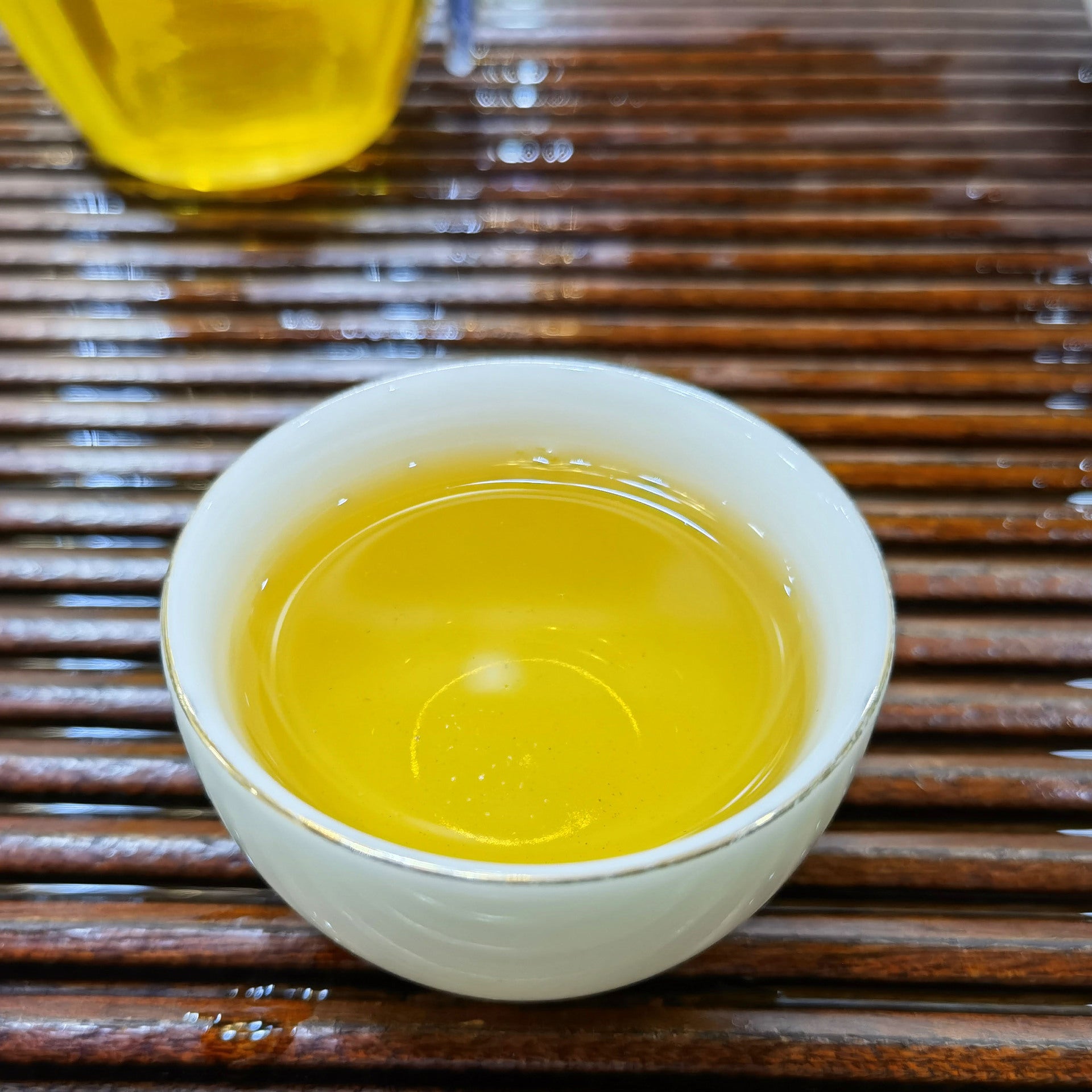 Golden Xigui sheng pu-erh tea liquor being poured into white porcelain cup — bright Lincang Chinese raw puerh infusion, bold orchid fragrance and mushroom notes
